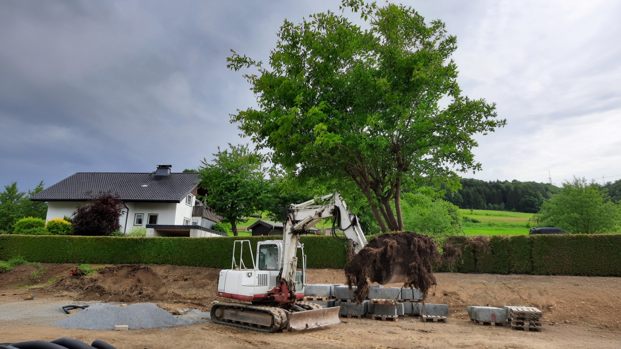 Minibagger auf einer Baustelle vor Hecke, Baum und Wohnhaus
